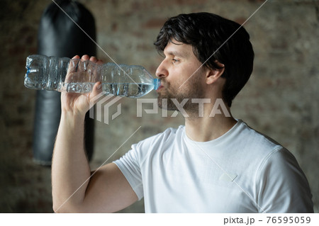 Man drinks water from bottle in gym. Health care and workout.  76595059