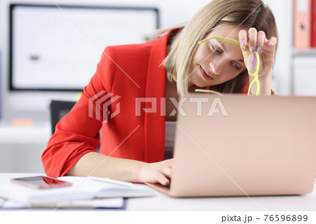 Tired woman sitting at laptop with glasses in her hands Tired woman sitting at laptop with glasses in her hands 76596899