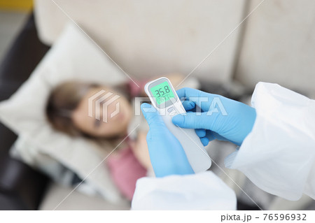 Doctor in gloves measuring temperature of woman with non contact thermometer at home closeup 76596932