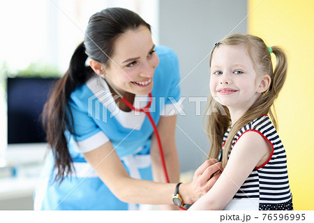 Smiling doctor listens with stethoscope to breathing of little girl 76596995