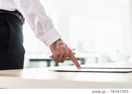 Businessman standing at his office desk pointing to a document 76597405