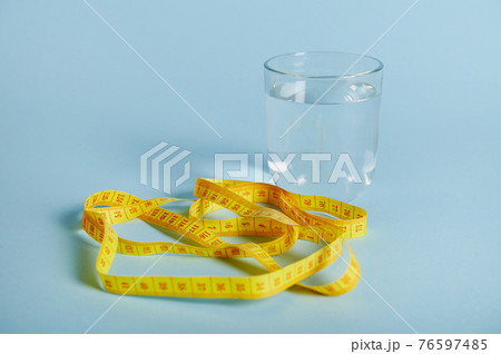 A glass with water and a measuring tape isolated on blue background with space for text 76597485