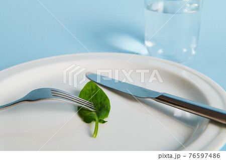 Closeup of a spinach leaf on a plate, fork, knife and glass with water on blue background. 76597486