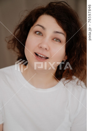 Portrait of a smiling brunette woman with curly hair in a white T-shirt.  76597846