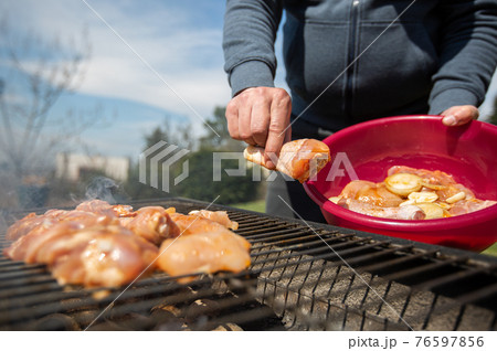 Man putting the RAW marinated chicken on a hot BBQ grill, concept of a grilling meat 76597856