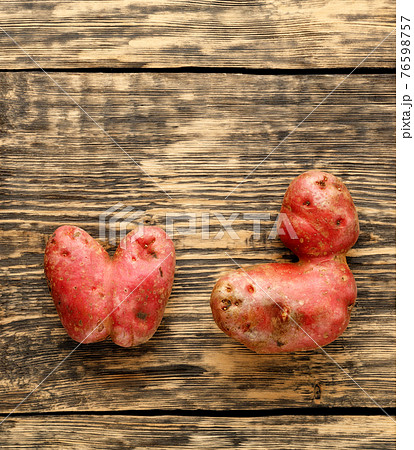 Vegetables or food waste concept. Ugly potato in the heart shape and letter shape on a brown wooden background. Top view, close-up. Vegetables or food waste concept. Ugly potato in the heart shape and letter shape on a brown wooden background. Top view, close-up. 76598757