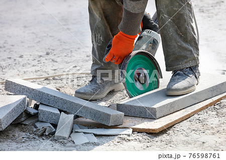 A builder holds a working electric saw with a diamond blade and cuts granite blocks in the background of the workplace. Close-up, blurred background. 76598761