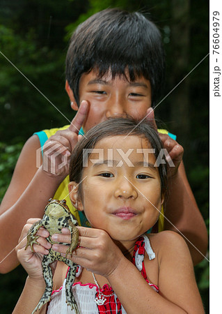 ヒキガエルを捕まえて喜ぶ少女と少年の写真素材