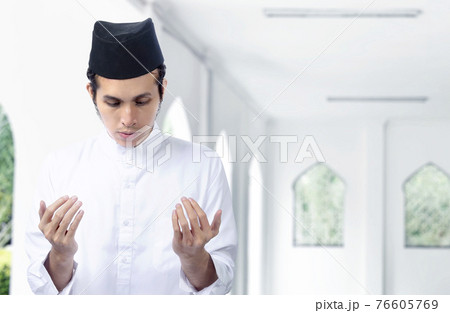 Asian Muslim man standing while raised hands and praying Asian Muslim man standing while raised hands and praying 76605769