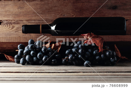 Bottle of red wine and a bunch of grapes on an old wooden table in the wine cellar. Bottle of red wine and a bunch of grapes on an old wooden table in the wine cellar. 76608999