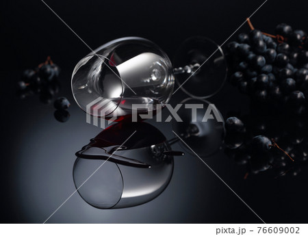 Blue grapes and wine glass with red wine on a black reflective background. 76609002
