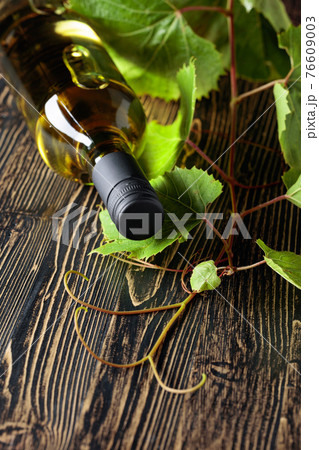 An unopened bottle of white wine and grapevine on an old wooden table. An unopened bottle of white wine and grapevine on an old wooden table. 76609003