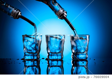 Vodka is poured from bottle into glasses with ice. Vodka is poured from bottle into glasses with ice. 76609004