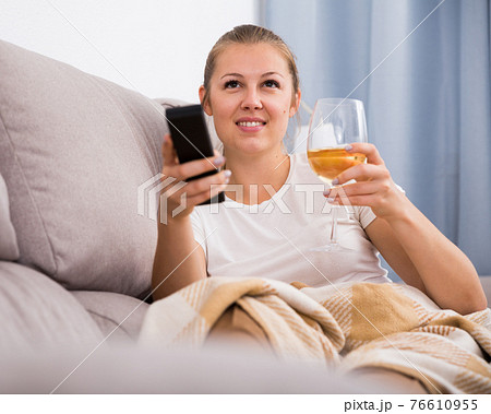 Young female is watching TV and sitting with white wine 76610955