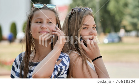 Two young girls talking on the phone on a summer day. 76618304