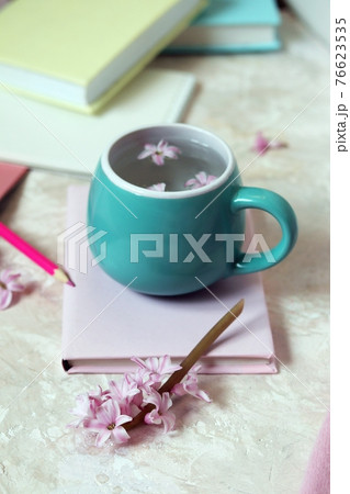 Cup with water and fresh hyacinth flowers, books, notepads, woolen pink sweater on a light background 76623535