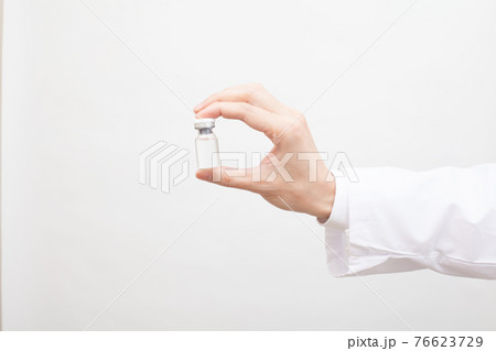 手に持たれたガラス瓶に入ったワクチン、液体の薬 76623729