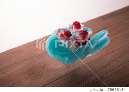 An ice sculpture in the shape of a hand holds frozen raspberries in ice cubes.The concept. An ice sculpture in the shape of a hand holds frozen raspberries in ice cubes.The concept. 76626184