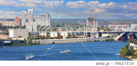 Panoramic cityscape of the Dnipro with cruising pleasure boats against the background of the Kyiv embankment, bright beautiful sky and city buildings. Panoramic cityscape of the Dnipro with cruising pleasure boats against the background of the Kyiv embankment, bright beautiful sky and city buildings. 76627319