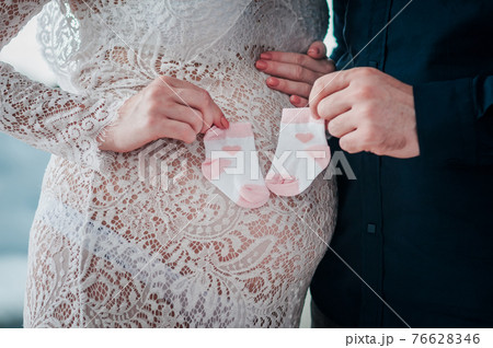 man and woman are holding in their hands small baby socks on a pregnant belly 76628346