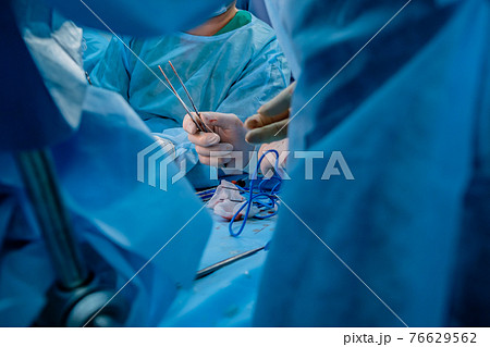 Bloodied surgeon's hands in sterile latex gloves holding surgical tweezers with traces of blood. Bloodied surgeon's hands in sterile latex gloves holding surgical tweezers with traces of blood. 76629562