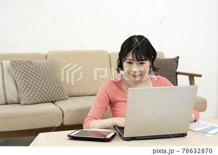 リビングでノートパソコンとタブレットを見る若い女性 76632870