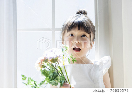 窓辺で花を持つ女の子の写真素材