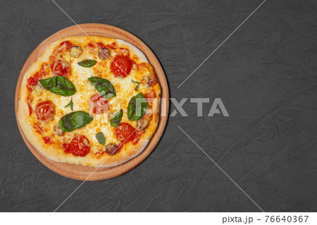 Pizza on wooden plate on black stone background. Cheese pizza with tomato, mozzarella and basil. Close-up photo. Copy space.  76640367