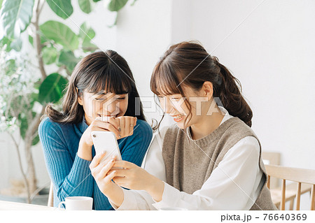 カフェでスマホを見る笑顔の女性2人組 76640369