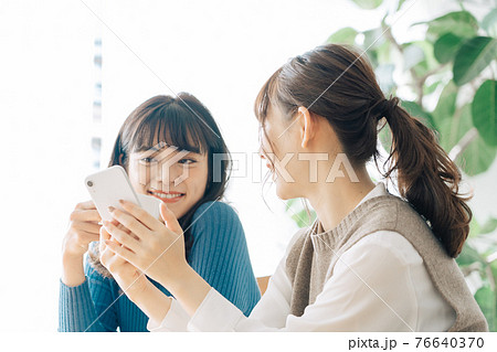 カフェでスマホを見る笑顔の女性2人組 76640370