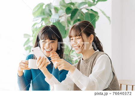 カフェでスマホを見る笑顔の女性2人組 76640372