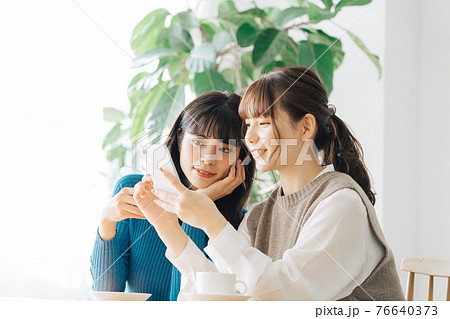 カフェでスマホを見る笑顔の女性2人組 76640373