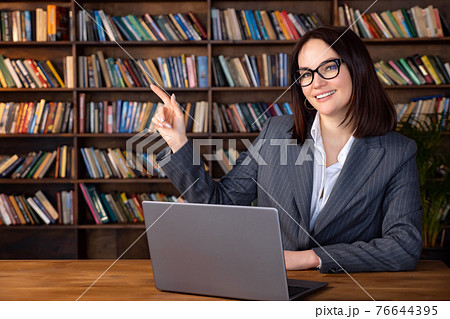 Woman in formal suit sitting at table with laptop pointing to copy space Woman in formal suit sitting at table with laptop pointing to copy space 76644395