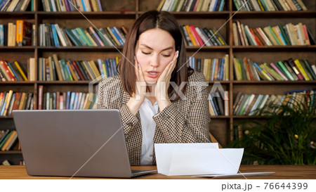 Businesswoman types on grey laptop looking at bank letter Businesswoman types on grey laptop looking at bank letter 76644399
