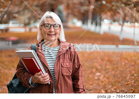 Smiling woman in casual clothes stands holding notebooks and backpack in city street. Smiling woman in casual clothes stands holding notebooks and backpack in city street. 76645097