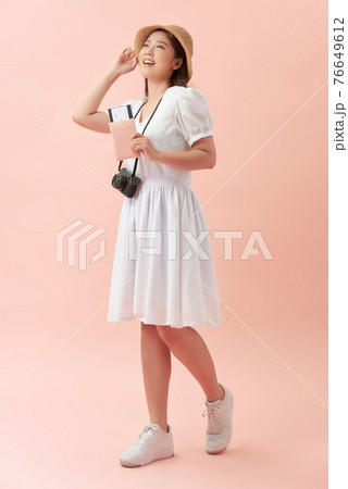 Full length of a happy young woman standing isolated over pink background, holding photo camera, showing passport with flight tickets 76649612