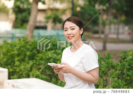 Photo of a happy smiling young woman in nature green park outdoors using mobile phone. 76649683