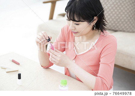 部屋でマニュキュアのふたを開ける若い女性 76649978
