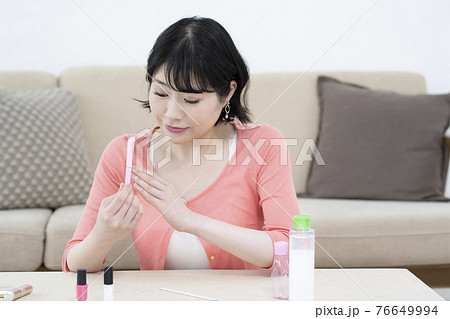 部屋で爪やすりで爪のケアをする若い女性 76649994