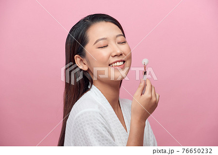 Close up of young woman with rose quartz face roller. She is doing beauty facial massage therapy 76650232