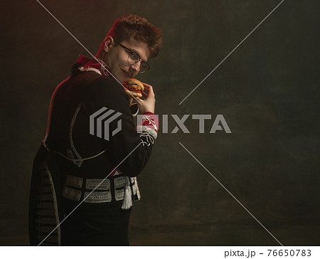 Young man in suit as royal person isolated on dark green background. Retro style, comparison of eras concept. Beautiful male model like historical character, monarch, old-fashioned. Young man in suit as royal person isolated on dark green background. Retro style, comparison of eras concept. Beautiful male model like historical character, monarch, old-fashioned. 76650783