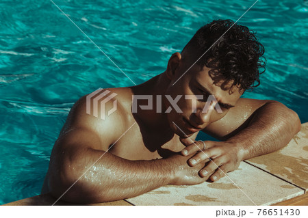 Strong face muscle male model in the open  summer shower on the vacation pool background with blue water on the nature beach on the sunset 76651430