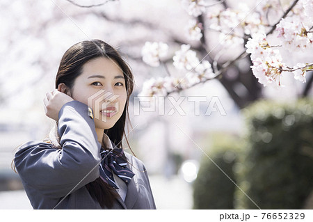 桜の前で風邪でなびく髪の毛を押さえる女子高生の写真素材