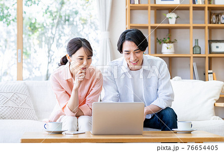 リビングでパソコンを見る若い夫婦 リビングでパソコンを見る若い夫婦 76654405