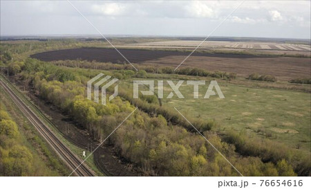 A railway track passing through the forest and field. Shooting from a height. Russian railway, taken from a height. 76654616