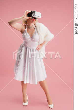 Portrait of young woman in white dress on coral pink background. Female model as a legendary actress. Pin up. Concept of comparison of eras, modern, fashion, beauty. Portrait of young woman in white dress on coral pink background. Female model as a legendary actress. Pin up. Concept of comparison of eras, modern, fashion, beauty. 76656273