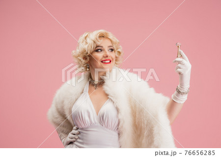 Portrait of young woman in white dress on coral pink background. Female model as a legendary actress. Pin up. Concept of comparison of eras, modern, fashion, beauty. 76656285