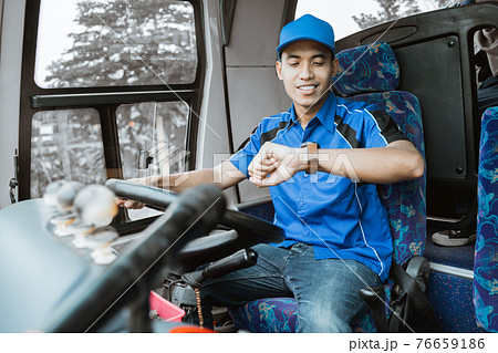 A male bus driver in blue uniform looks at his watch while sitting driving A male bus driver in blue uniform looks at his watch while sitting driving 76659186