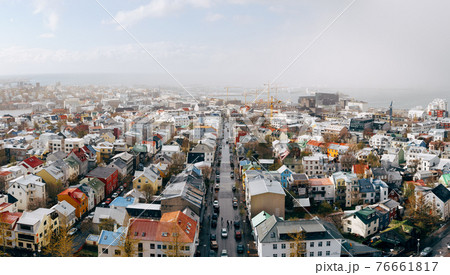 The snow covered rooftops of Reykjavik, historic capital city of Iceland. Traditional houses, aerial view, with the coastline, sea and mountains beyond. 76661817