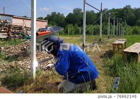 A fence installer welds a metal profile to a new fence post. A fence installer welds a metal profile to a new fence post. 76662149